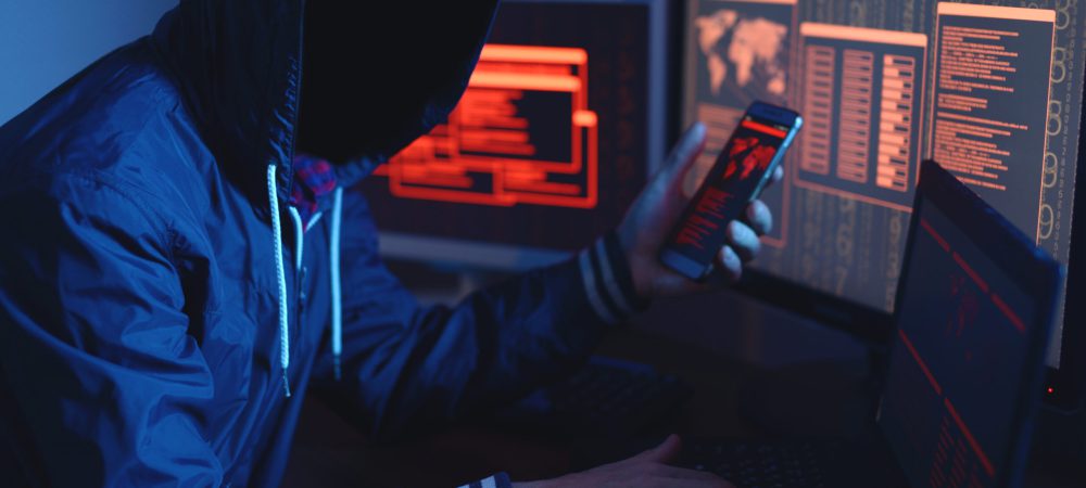 An anonymous hacker with no face typing the code tries to hack the system and steal accesses on the background screens in neon light. The concept of cybersecurity